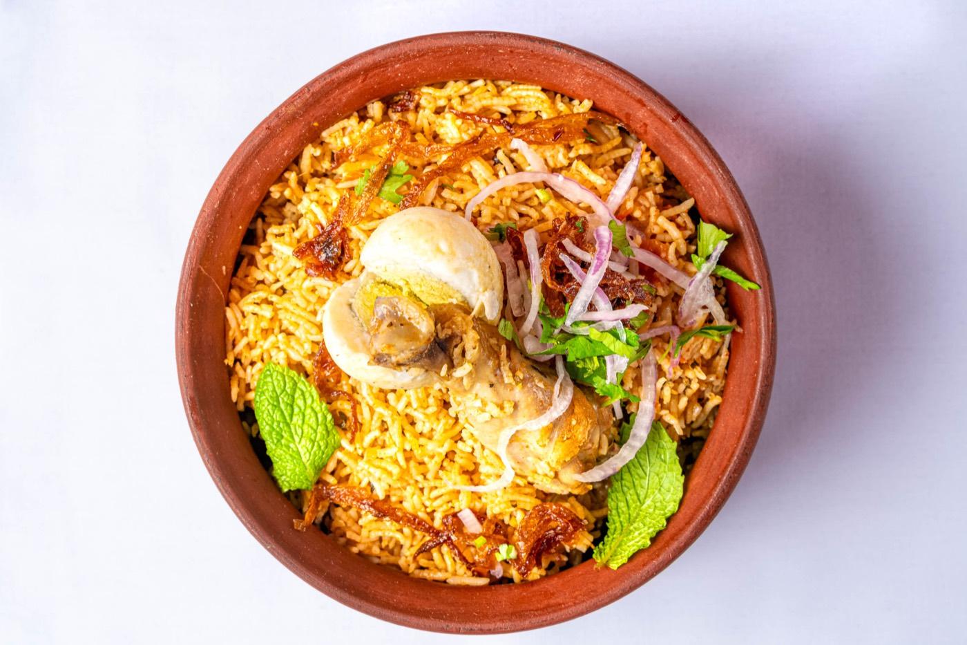 Chicken dum biryani in a clay pot topped with boiled egg, fried onions and mint